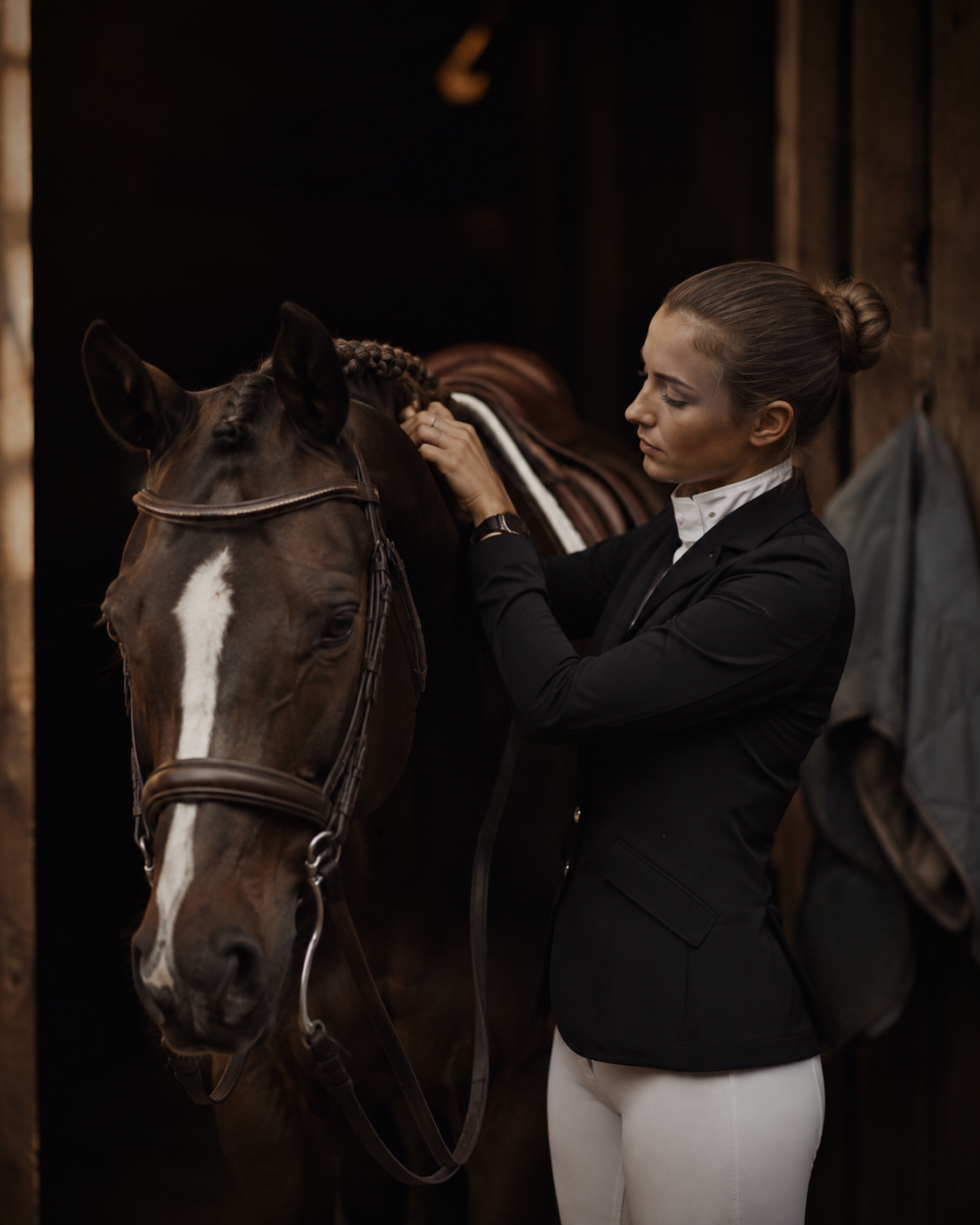 Rider carefully preparing her horse at the stable doorway